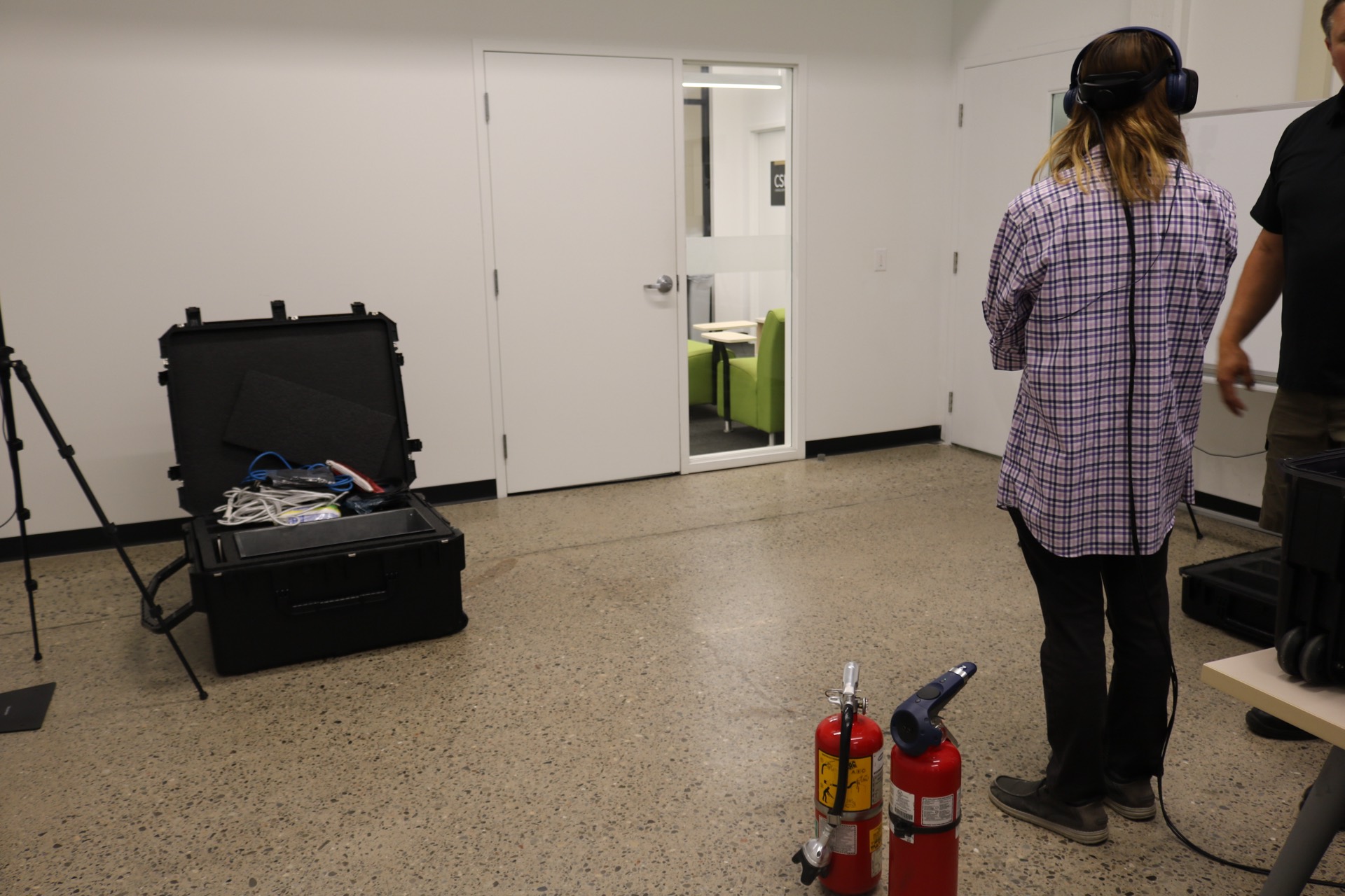 A tester wearing a VR headset works an instrumented fire extinguisher during a testing session with Catapult Tactical XR, with real extinguishers staged on the floor