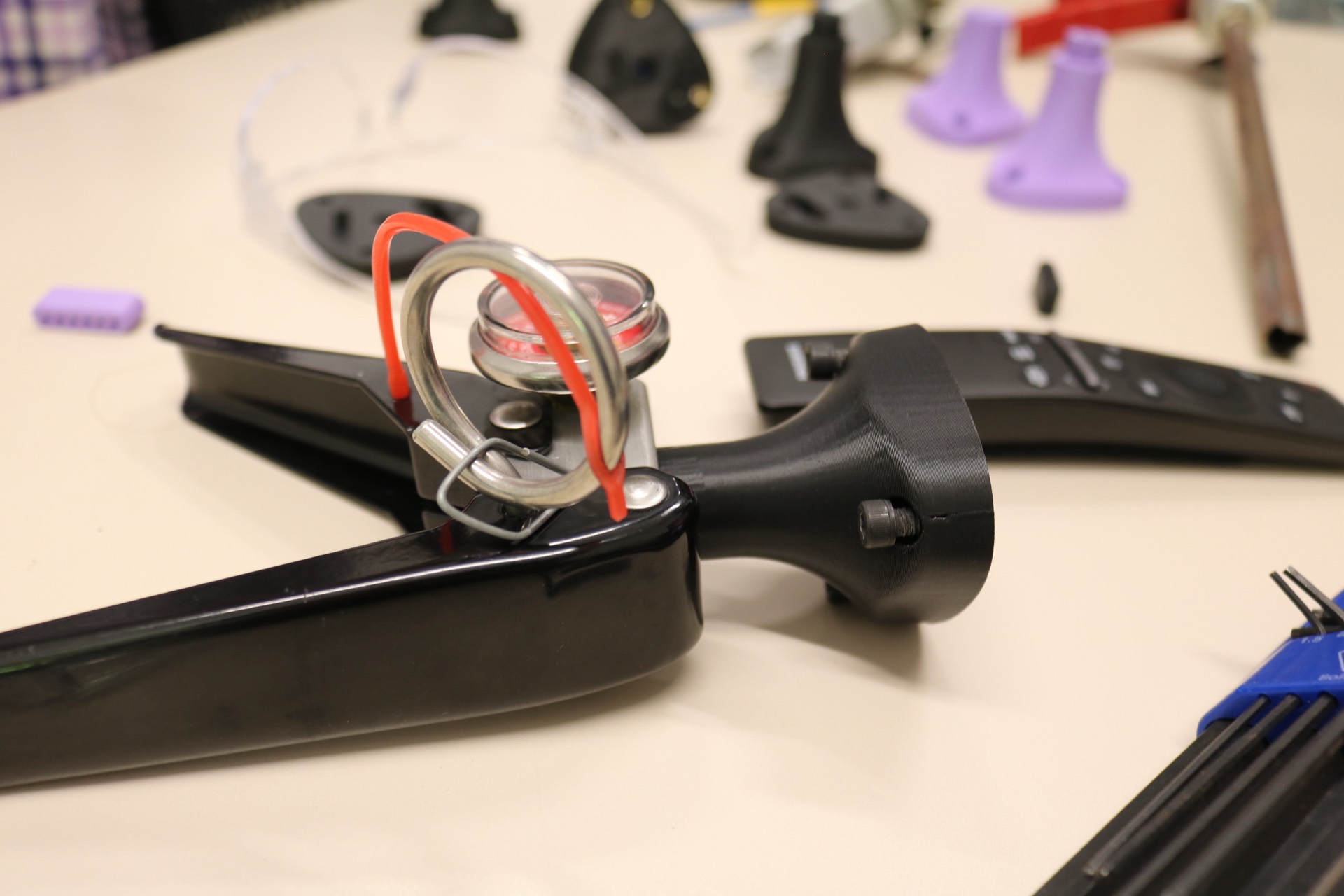 Close-up of an instrumented fire extinguisher handle with the safety pin and trigger intact, an AR sensor mounted above, and a 3D printed nozzle base