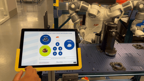 A visitor selecting a coffee pod on the Ignition HMI tablet while the YuMi cobot waits behind it