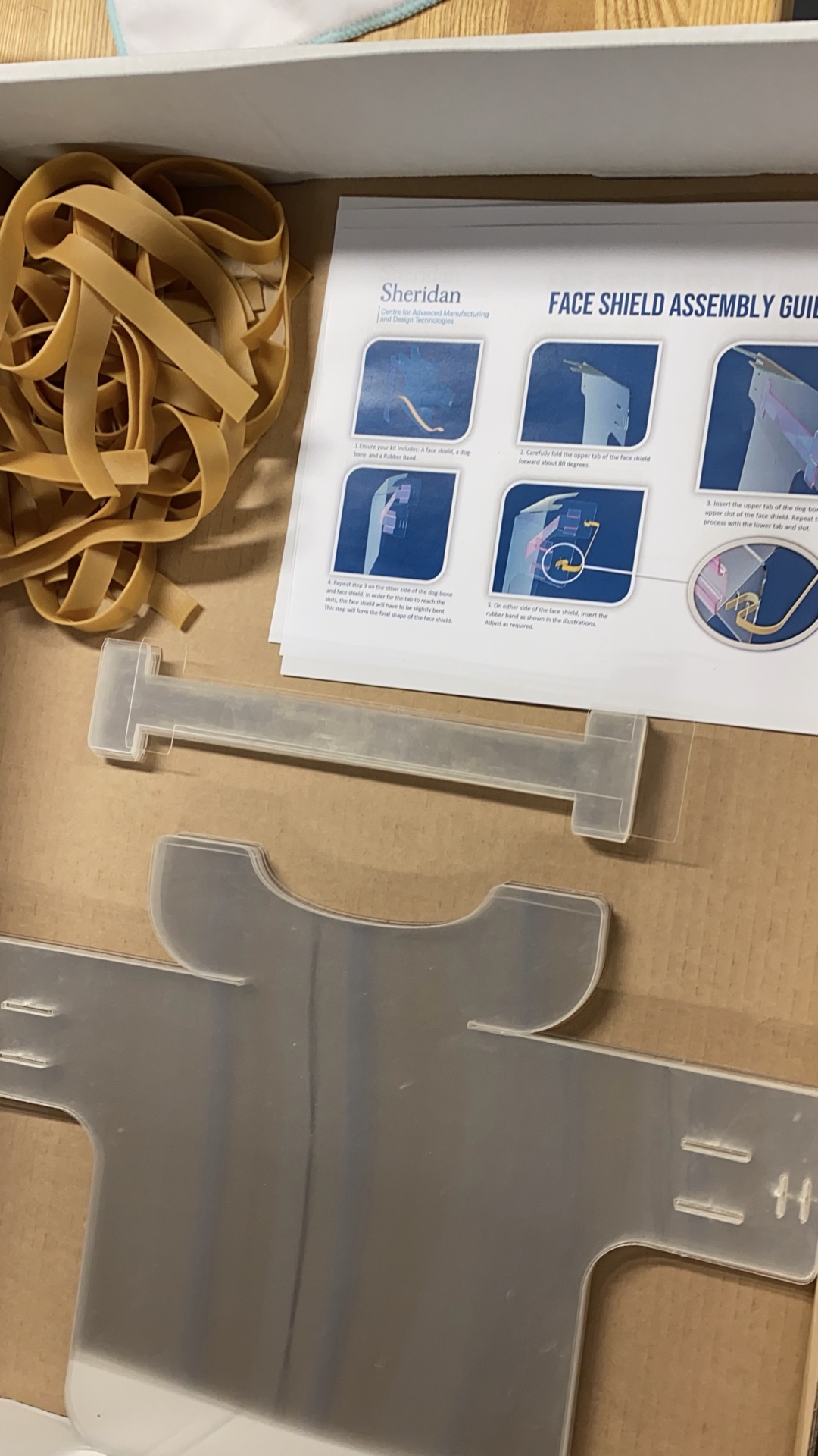 Flat-packed PETG face shield kit with assembly guide, rubber bands, and clear shield sheet