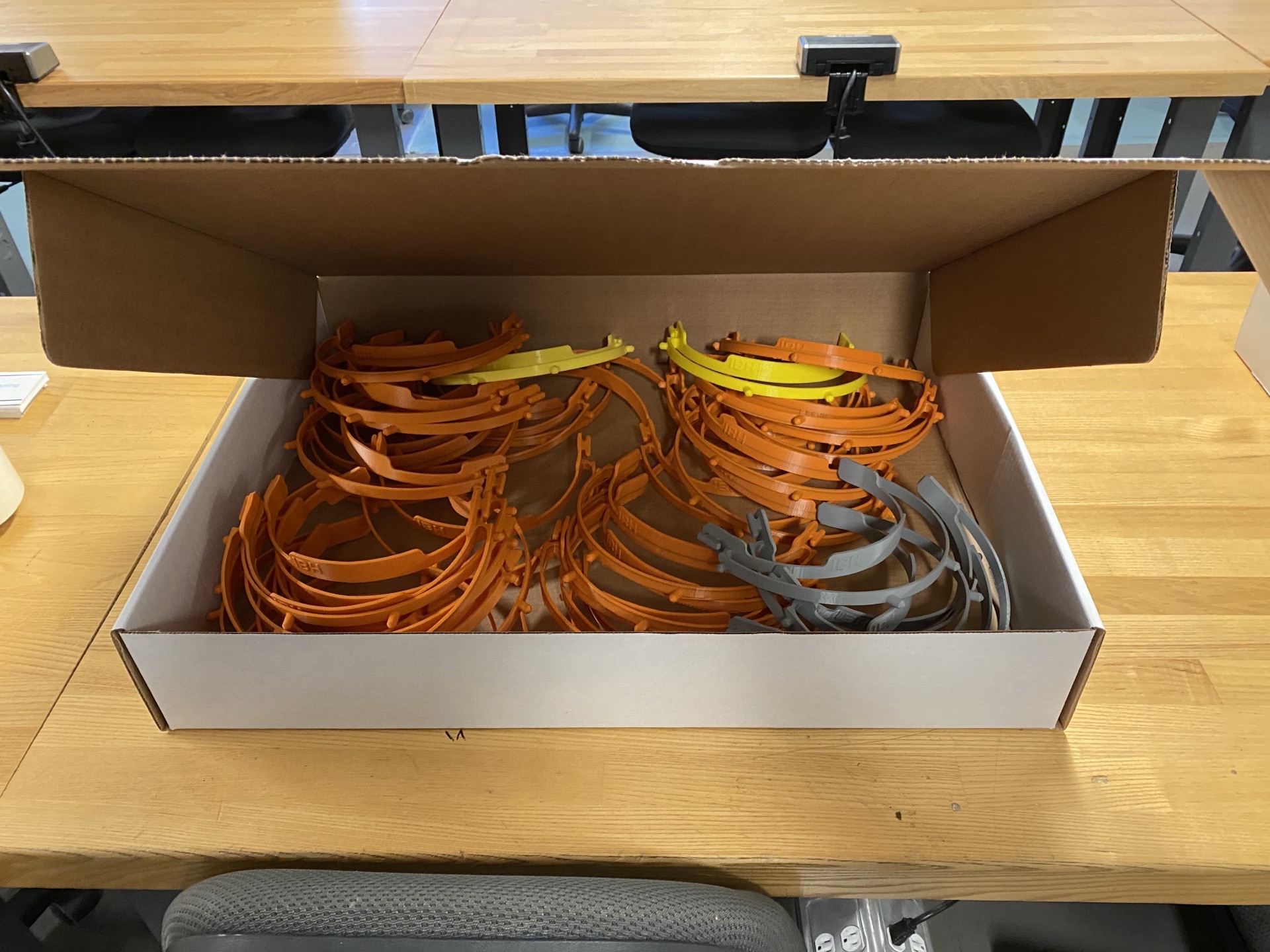 Box of 3D printed headband frames in orange, yellow, and grey