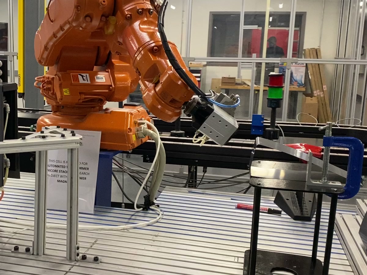 The custom magnetic end-effector mounted to the robot wrist, extended toward the placement station