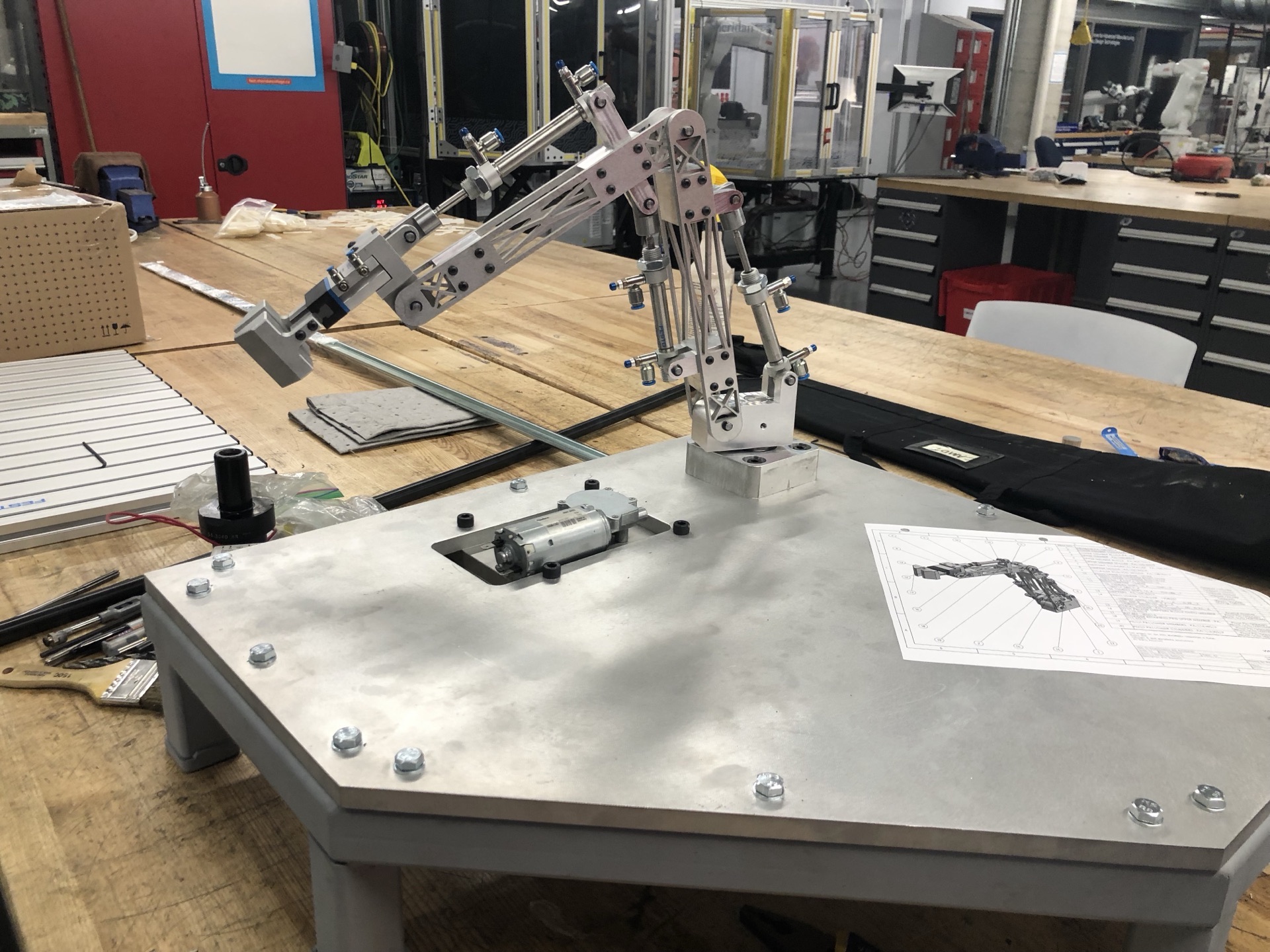 Built Polymechanics pneumatic arm sitting on its base plate with the printed drawing alongside